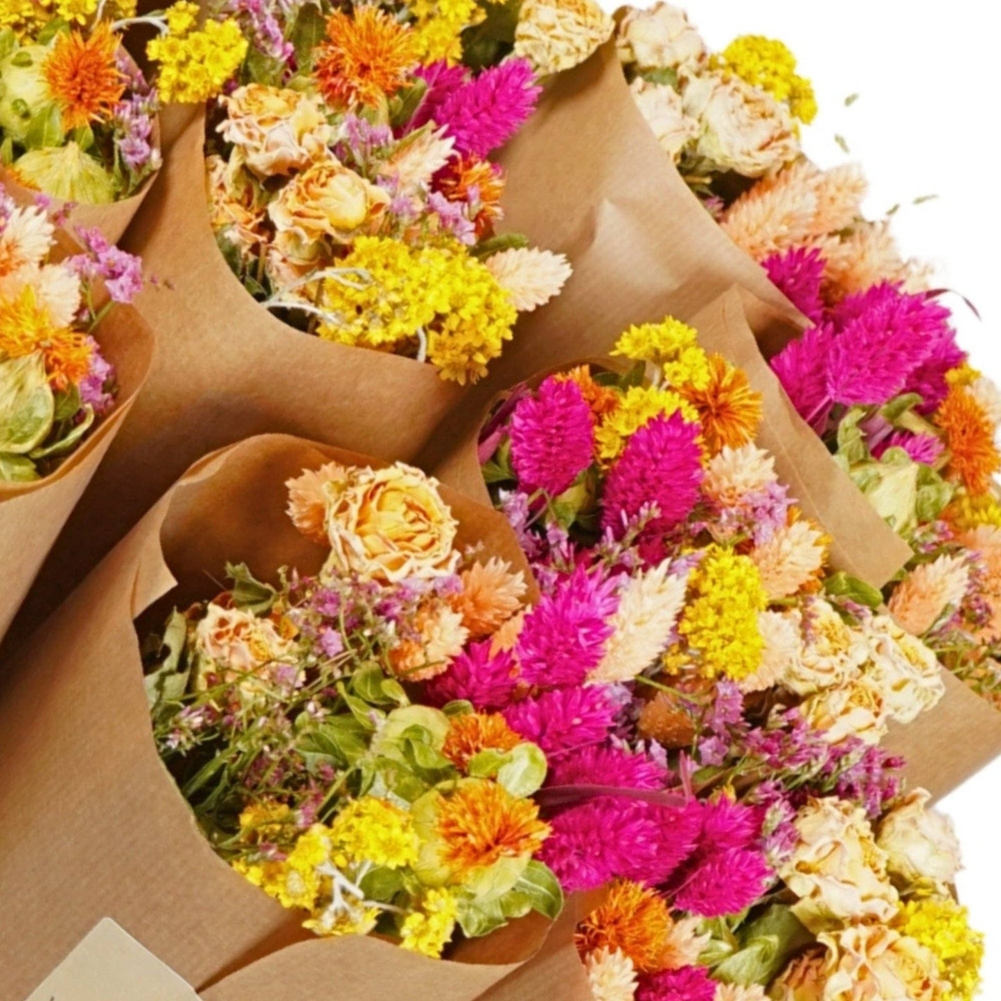 Sträuße aus leuchtenden Trockenblumen in Gelb-, Orange-, Rosa- und Beigetönen sind kunstvoll in braunes Kraftpapier eingewickelt und eng aneinandergebunden – jeder einzelne Strauß unterstreicht den bezaubernden Charme der Kollektion „Wildflowers by Floriette | ‚Summer Crush‘ – Sommer-Bestseller-Trockenblumen“.