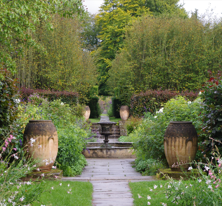 Ein von großen Terrakotta-Urnen gesäumter Steinweg führt durch den vielfältigen Garten von Yorkshire zu einem stufenförmigen Steinbrunnen, der im Rahmen des Afternoon Tea am Di., 16.2.2027 | 14.30 – 15.30 Uhr im Mittelpunkt steht.