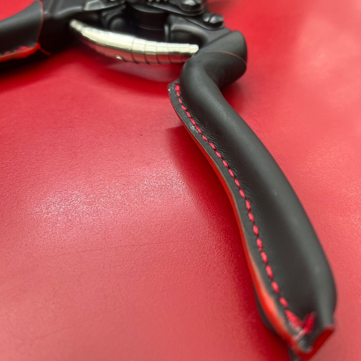 Nahaufnahme eines schwarzen Fahrradbremshebels mit roter Naht vor leuchtend rotem Hintergrund. Der glatte, geschwungene Griff und die freiliegenden Metalldetails spiegeln die Präzision eines Felco 8 - PREMIUM von Felco wider.