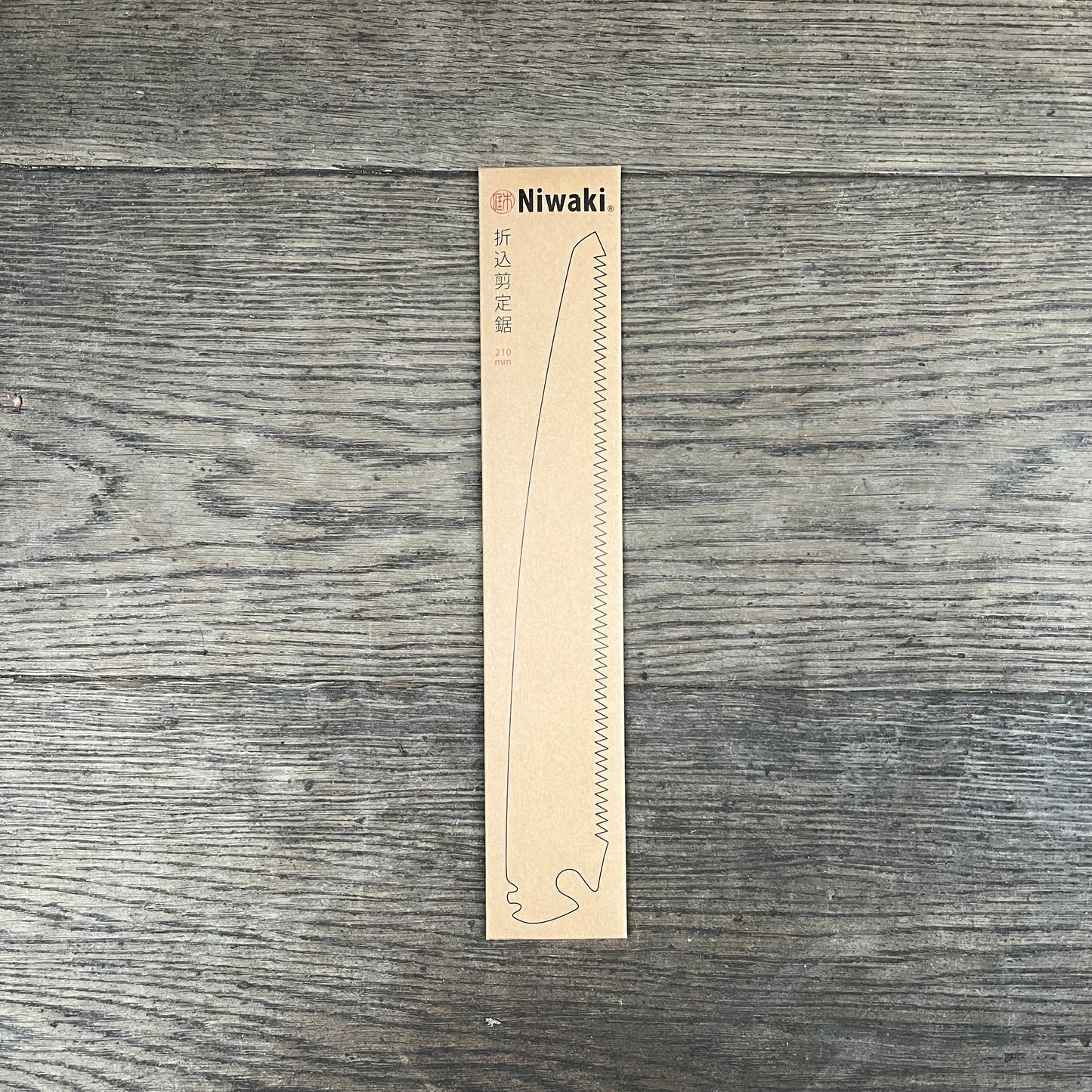 Eine rechteckige Pappverpackung mit der Aufschrift Niwaki, auf der die Niwaki | Ersatzklinge für Niwaki Gartenschere GR 210 abgebildet ist, mit einer Linienillustration, japanischen Schriftzeichen und "210" auf einer Holzoberfläche.