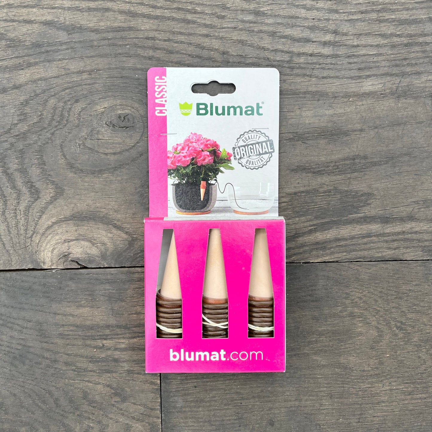 Blumat | 'Classic' Praktische Bewässerung für Zimmer- und Balkonpflanzen: Drei Selbstbewässerungs-Kegel mit brauner Basis in pinker Verpackung, Label mit Blumat-Logo und Topfpflanze mit pinken Blüten auf Holzhintergrund.