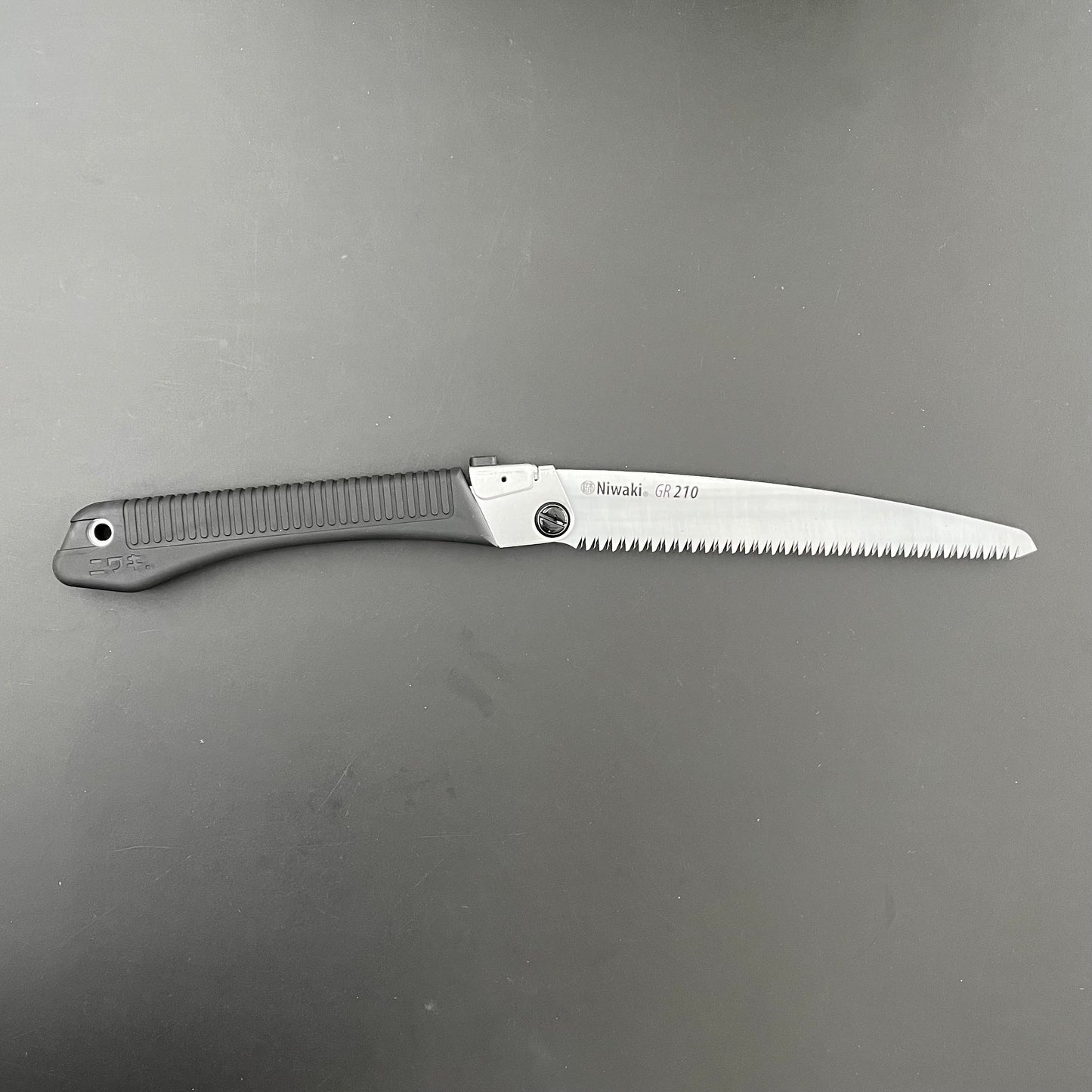 Die Niwaki | 'GR 210 Folding Saw' Klappsäge hat einen schwarzen Griff und eine silberne Klinge mit der Aufschrift "Niwaki GR-210", mit scharfen Zähnen - perfekt als Outdoorsäge oder für präzise Gartenschnitte. Teilweise geöffnet vor einem dunklen Hintergrund abgebildet.