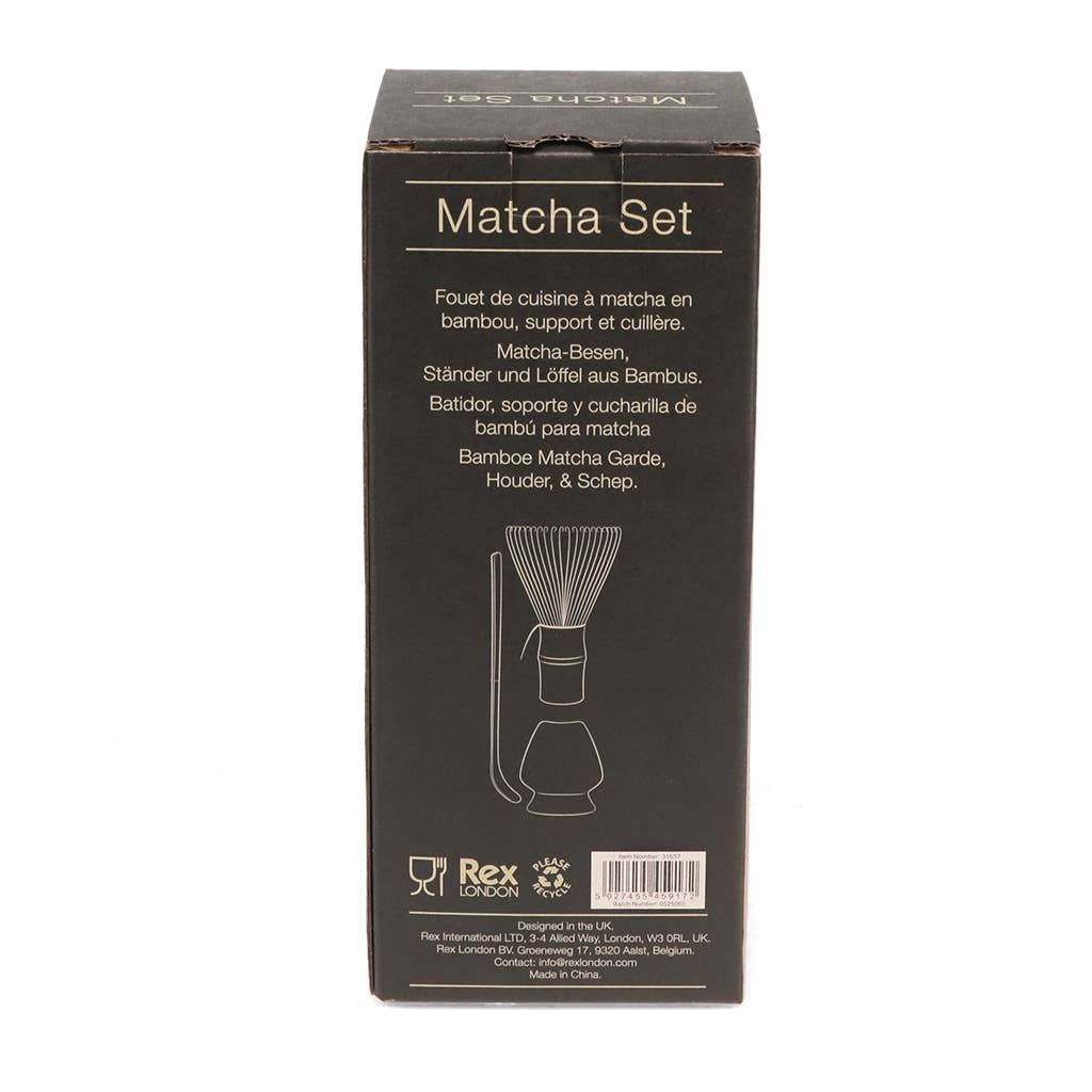 Eine schwarze Schachtel mit der Aufschrift "Rex | Handgefertigter Matcha Besen & Ständer im Set" von Rex Europe, mit goldenem Text und einer Abbildung von Bambusbesen, Halter und Löffel - ideal für die japanische Tee-Zeremonie. Die Beschreibung in mehreren Sprachen ist auf der Verpackung zu finden.