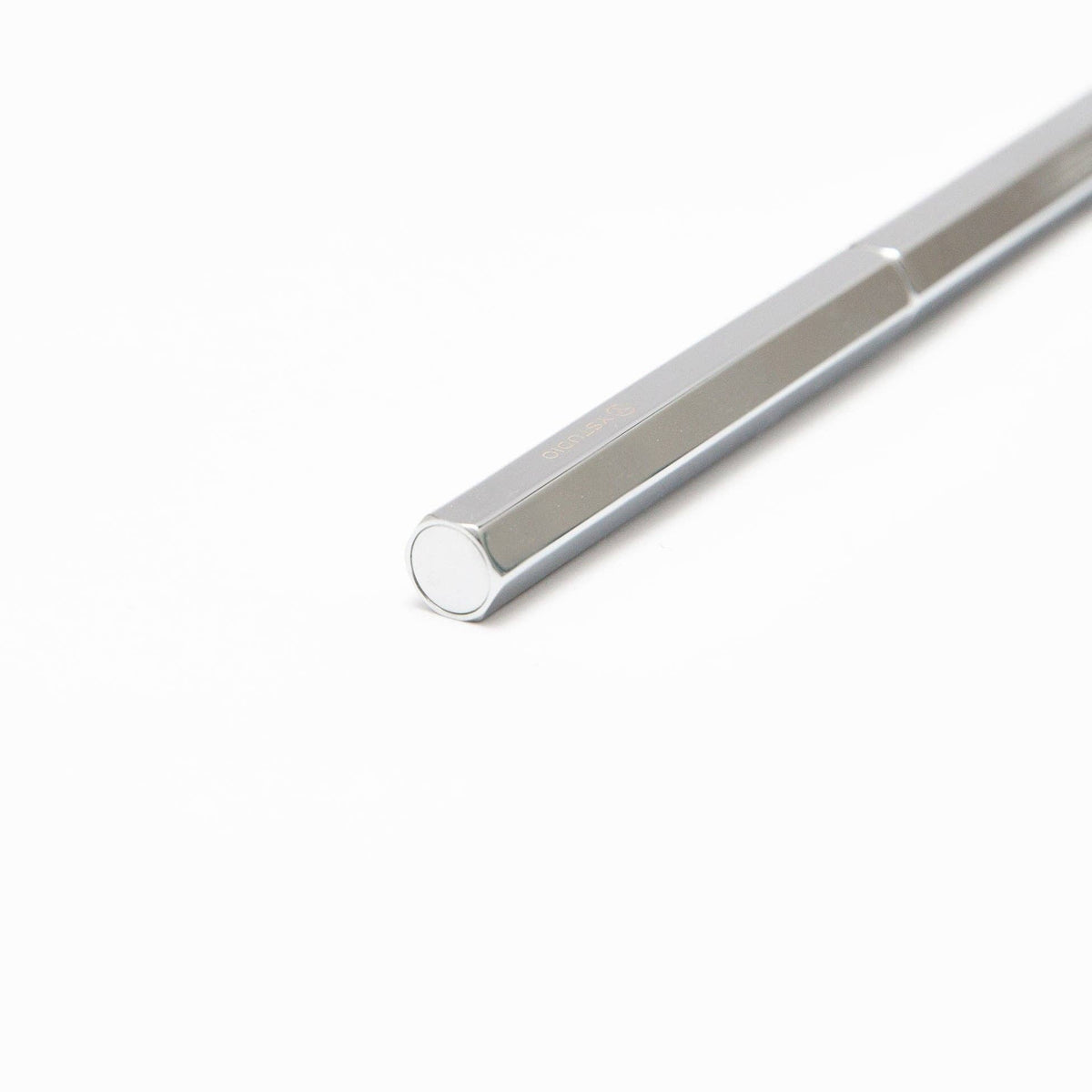 Eine Nahaufnahme des ENTREPÔT YSTUDIO „Klassischer Revolve“-Kugelschreibers Slim in glänzendem Silber, der sich durch einen glänzenden sechseckigen Metallkörper mit glänzender Metalloberfläche auszeichnet und diagonal auf einem weißen Hintergrund platziert ist.