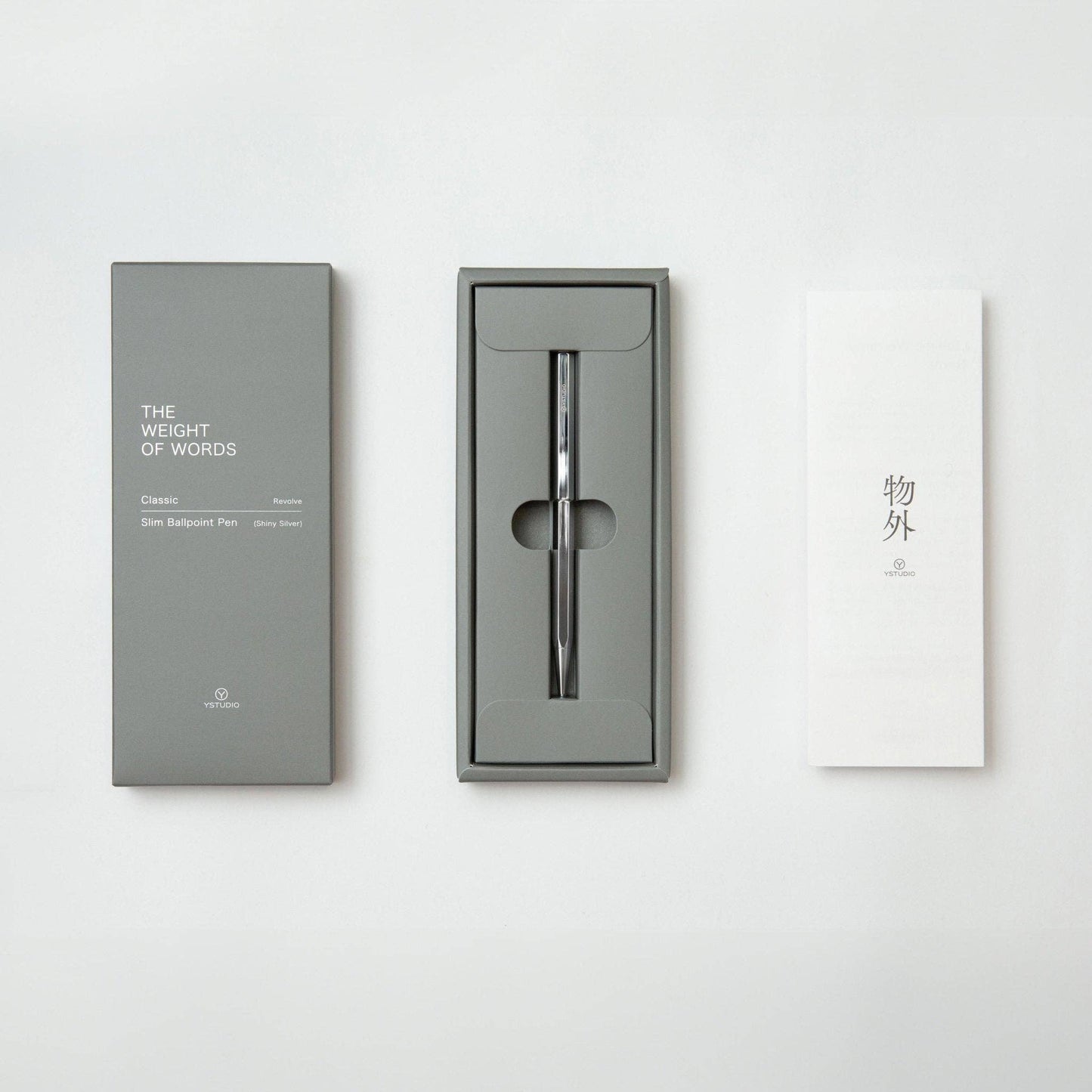 Der YSTUDIO | Klassischer Revolve Kugelschreiber Slim (Glänzendes Silber) von ENTREPÔT liegt elegant in einer grauen THE WEIGHT OF WORDS-Box samt Anleitung mit asiatischen Zeichen - alles stilvoll auf weißem Grund präsentiert.