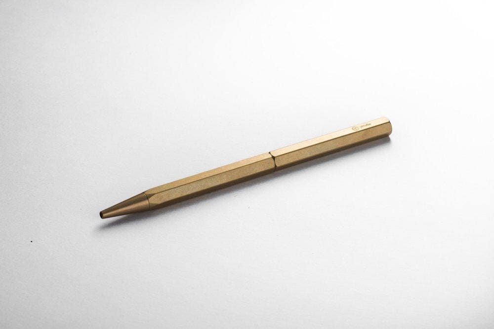Der ENTREPÔT YSTUDIO Klassischer Revolve Kugelschreiber Schlank in Gold mit sechseckigem Design ruht diagonal auf einer schlichten weißen Fläche.