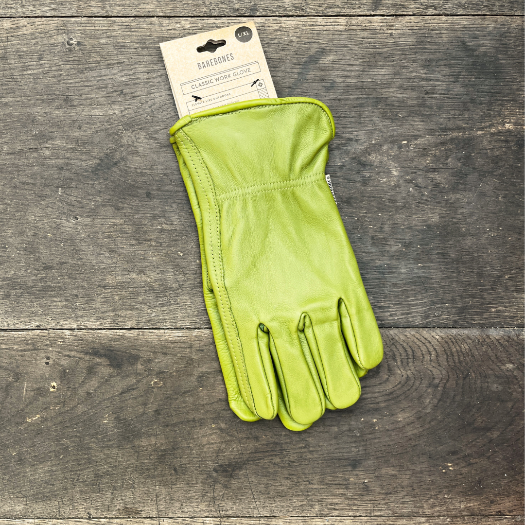 Ein Paar olivfarbene „Barebones“ | Gartenhandschuhe aus Büffelleder (XS–XL) der Königlichen Gartenakademie liegt auf einer Holzunterlage und ist mit einem Kartonetikett versehen, auf dem „Classic Work Glove“ steht – ideal für alle Ihre Gartenarbeiten.