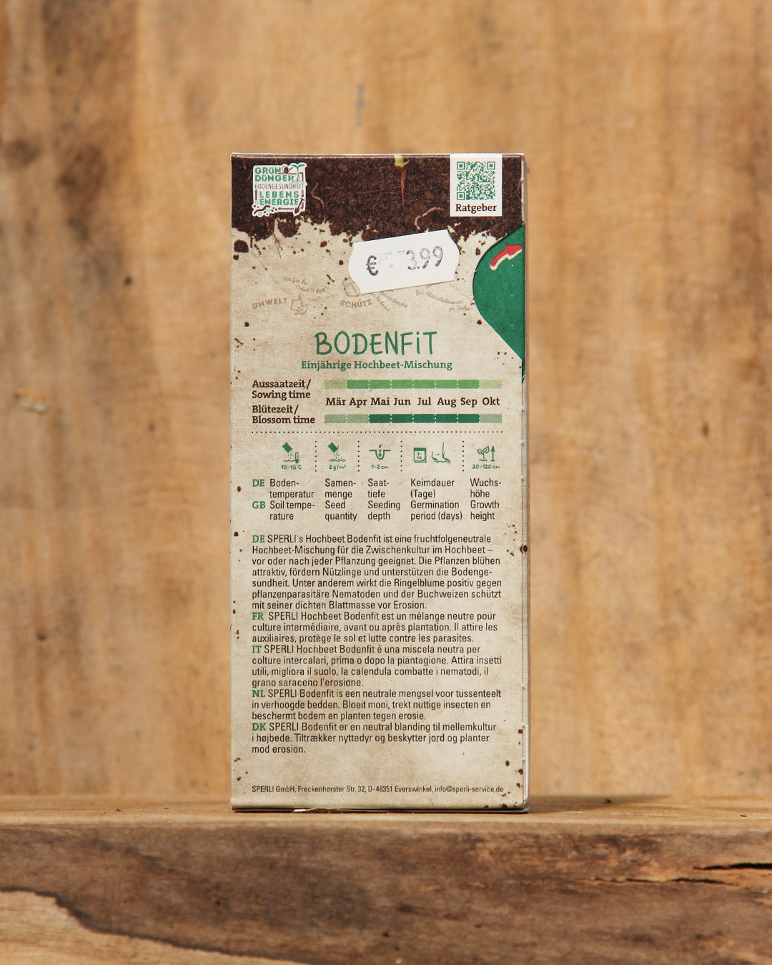 Eine rechteckige Sperli's-Schachtel mit der Aufschrift Hochbeet Bodenkur 'Bodenfit' 200 g enthält deutsche Pflanzinformationen, einen 3,99 €-Aufkleber, Aussaatsymbole und ein erdiges Gründüngermischung-Design auf einem natürlichen Holzhintergrund.