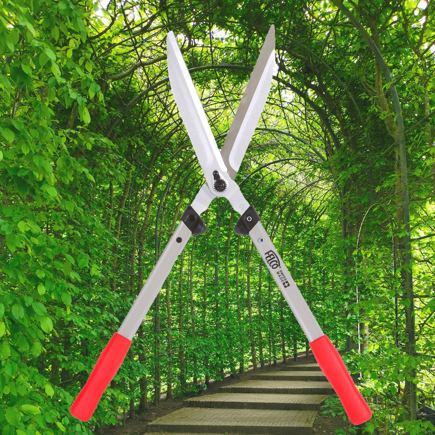 Die Felco 250-63 Heckenschere von Felco mit ergonomisch geformten Griffen in Rot ist vor einem grünen, belaubten Torbogen und einem gepflasterten Weg abgebildet und liefert präzise Ergebnisse für jede Gartenarbeit.