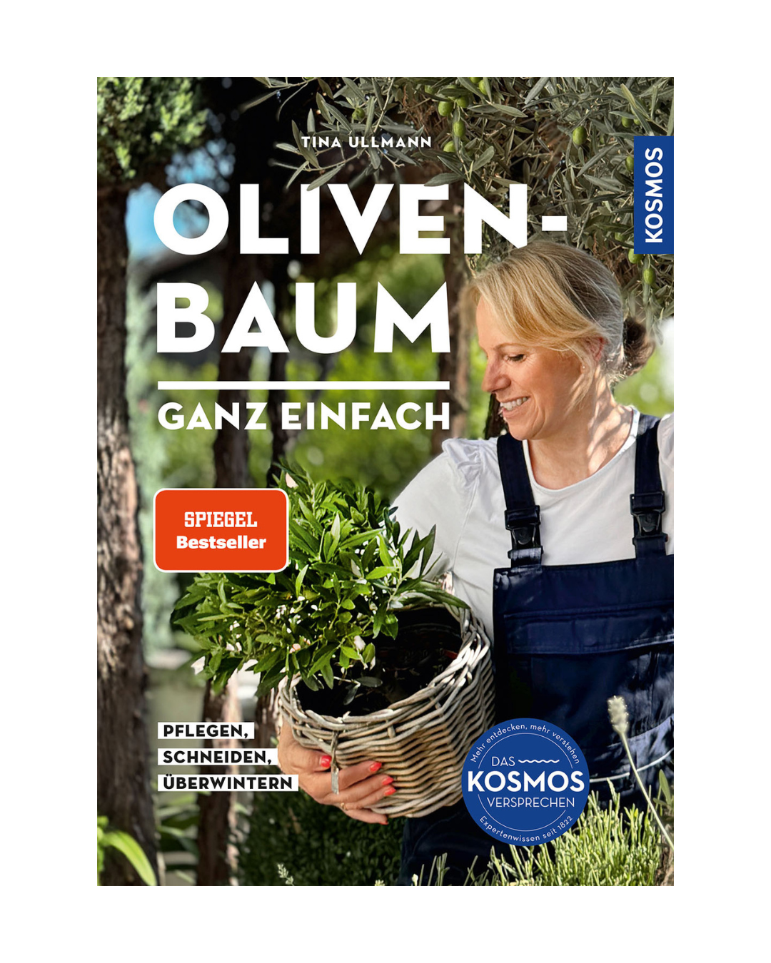 Eine lächelnde Frau in Latzhose hält einen Olivenbaum in einem Korb. Das Buch "Olivenbaum ganz einfach | Pflegen, schneiden, überwintern" aus dem Kosmos Verlag ist ein Spiegel-Bestseller mit fachkundigen Tipps zur Pflege und Überwinterung, alles in deutscher Sprache.