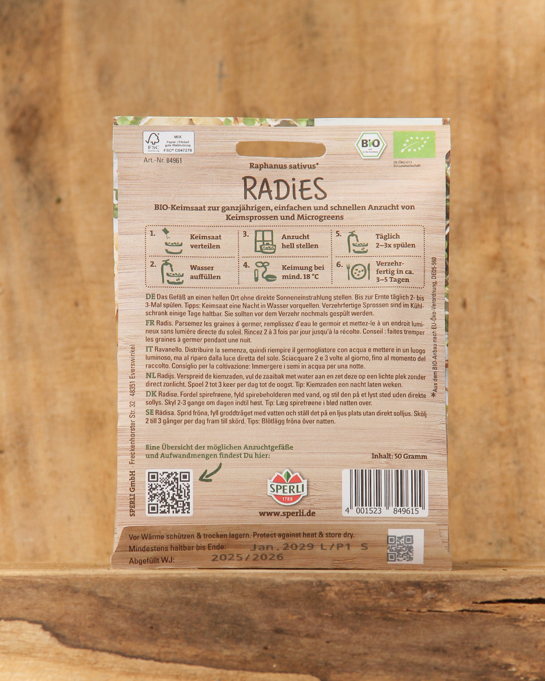 Eine Packung Sperli's | Bio Keimsprossen Saat 'Radies' steht aufrecht auf einer Holzunterlage. Auf der Rückseite finden sich eine ausführliche Anbauanleitung, Logos der Bio-Zertifizierung, ein Strichcode und grüne Akzente - Vitaminbomben für die Küche.