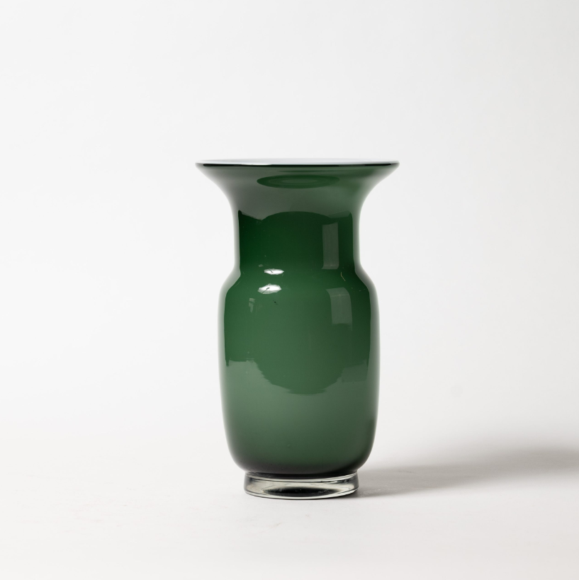 Die Des Pots Grün Vase aus Glas in Kelchform (H 27 cm, Ø 17 cm) mit glänzender, reflektierender Oberfläche und leicht zulaufendem Sockel steht auf weißer Fläche vor schlichtem Hintergrund.