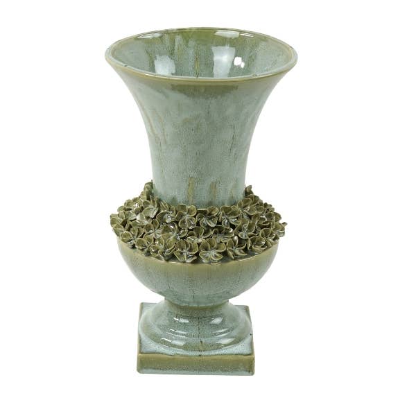 Wir präsentieren die „Amphore“ von Werner Voß: eine mediterran inspirierte Vase aus grünem Steingut (25 x 41,5 cm) mit dekorativen floralen Details, die den mittleren Bereich umgeben, einem breit auslaufenden Rand und einem eleganten quadratischen Sockel.