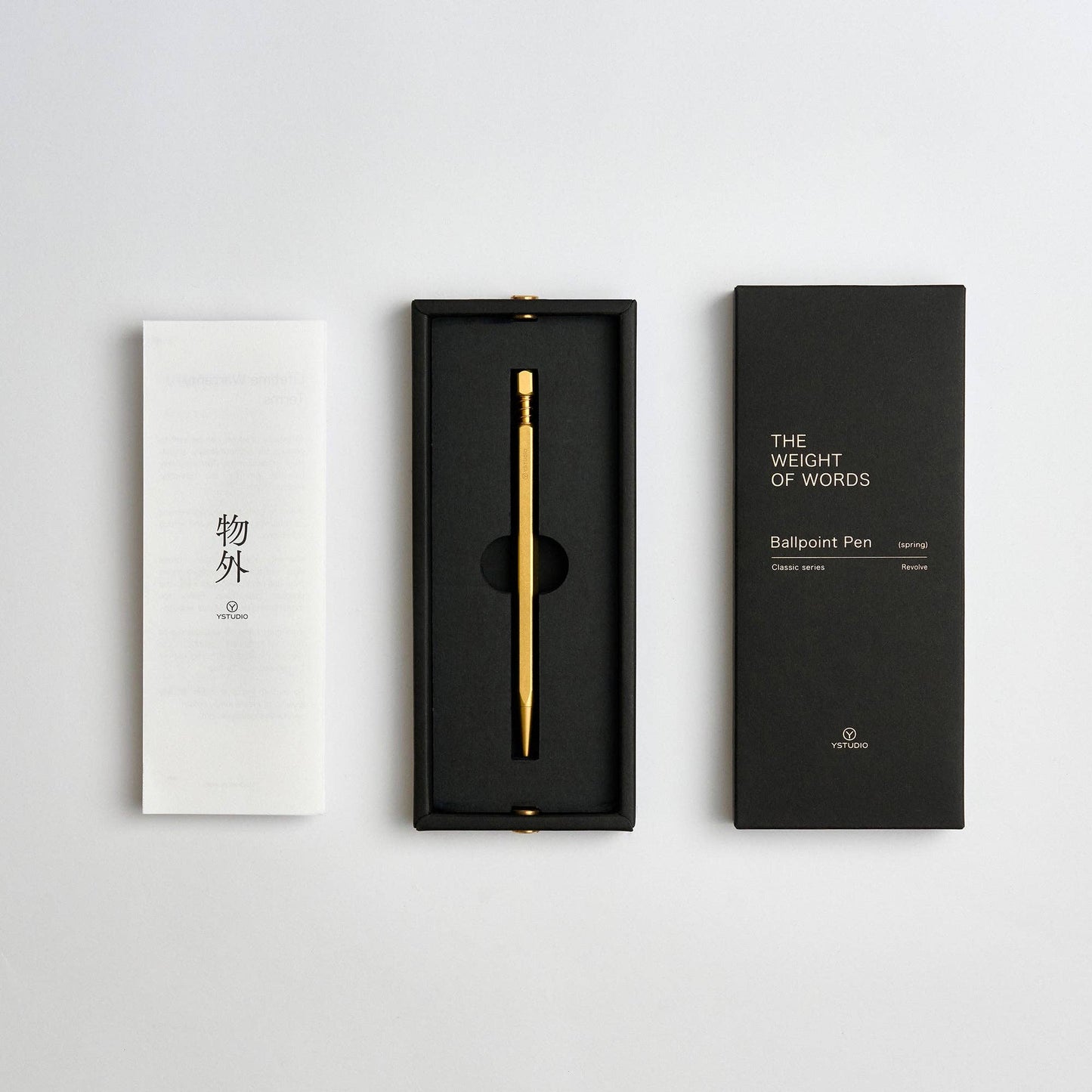 Der YSTUDIO | Klassischer Revolve Kugelschreiber Feder (Messing) von ENTREPÔT - ein langlebiger Goldkugelschreiber mit Federkappenstruktur - kommt in einer schwarzen Box mit einem weißen Faltblatt mit asiatischen Schriftzeichen und einem Booklet "The Weight of Words Ballpoint Pen".