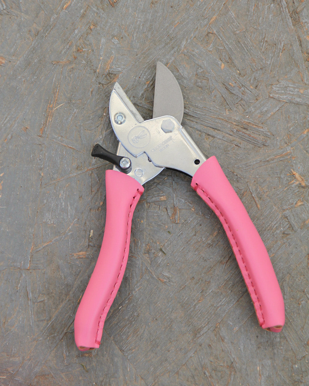 Ein Paar der Gartenschere "Pink Tulip" von Chop Chop Bloom, inspiriert von der Initiative Brustkrebs, ruht auf einer strukturierten Holzoberfläche.