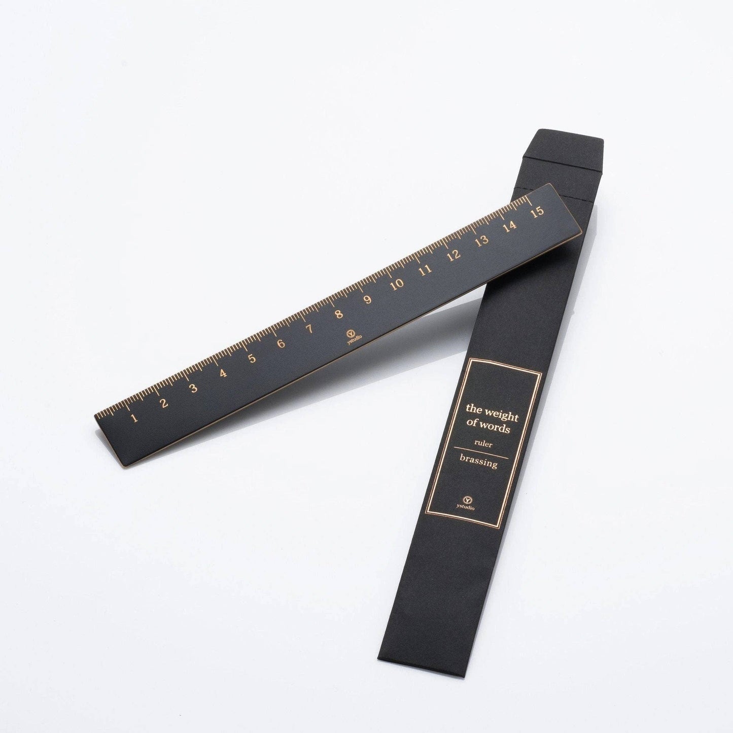 Ein schwarz-goldener YSTUDIO | Klassischer Reflect Lineal von ENTREPÔT ruht neben dem passenden schwarzen Etui mit der Aufschrift "the weight of words ruler brassing" auf weißem Hintergrund - ein elegantes Büroaccessoire für Ihren Schreibtisch.