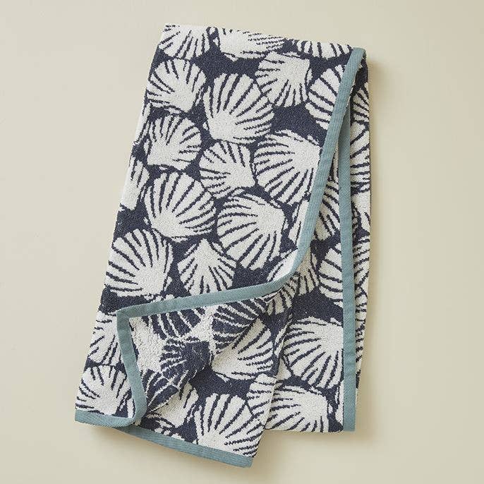 Ein gefaltetes Sylvie Thiriez Badetuch "Baleares Muschel" (70 x 150 cm) mit einem marineblauen und weißen Muschelmuster mit hellblauem Rand wird auf einer neutralen Fläche präsentiert.
