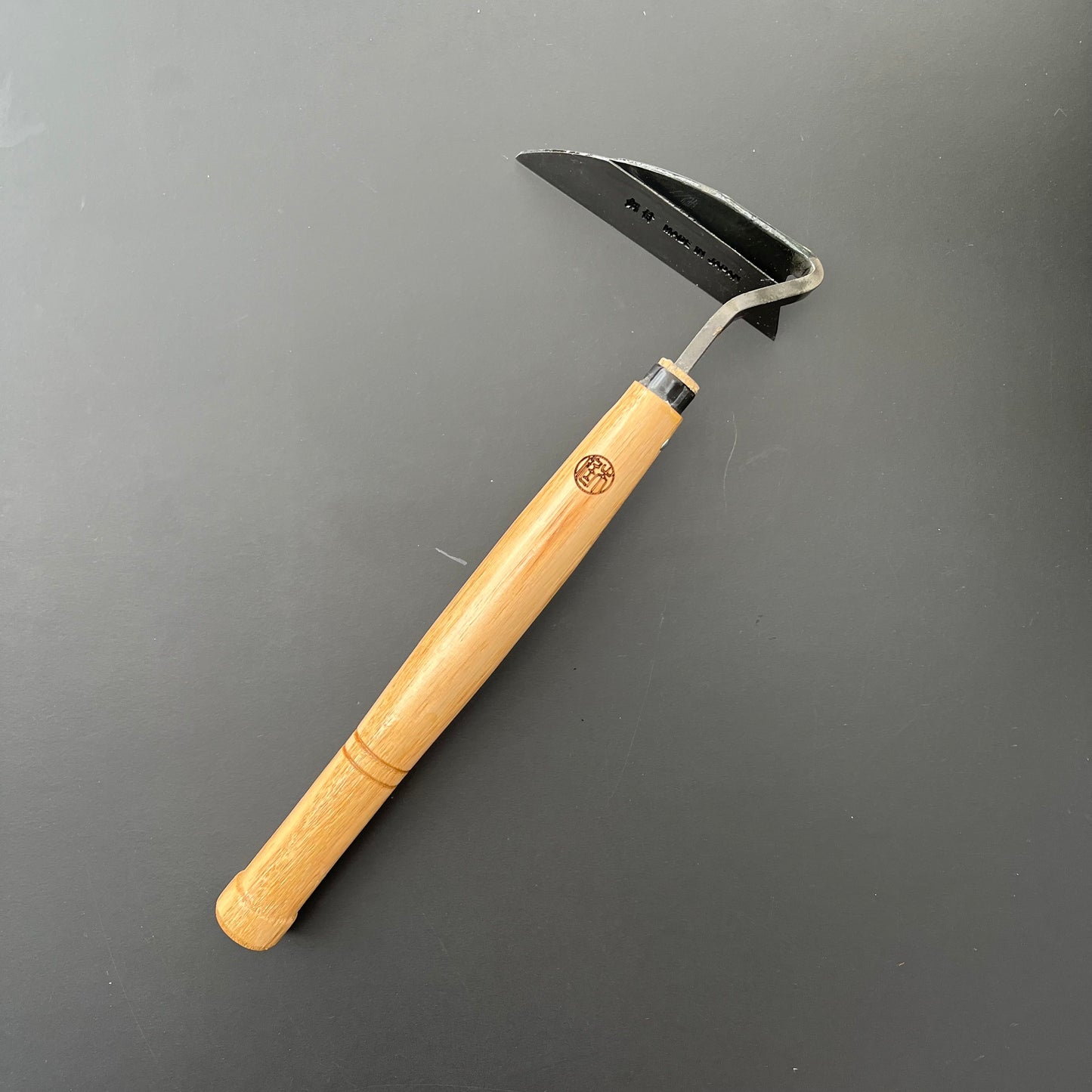 Die Niwaki 'Unkrauthacke' Jäthacke für Rechts- und Linkshänder ist mit einer gebogenen Metallklinge und einem Holzstiel ausgestattet, die sich perfekt zum Entfernen von Unkraut eignen, und steht auf einem schlichten schwarzen Hintergrund.