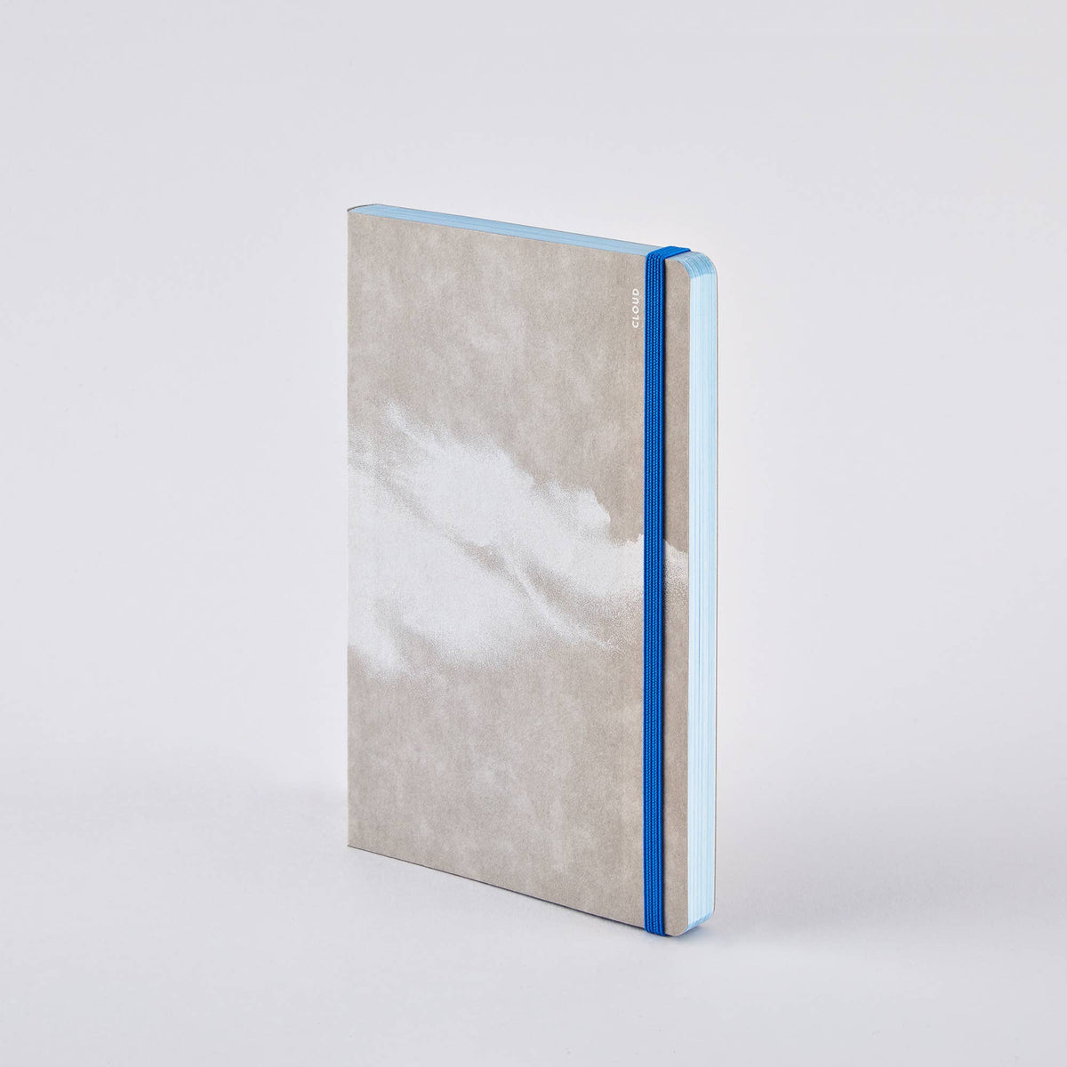 Ein geschlossenes nuuna „Cloud Blue“-Inspirationsbuch in Größe M mit einem grau-weiß marmorierten Einband, das mit einem blauen Gummiband verschlossen ist, steht aufrecht vor einem schlichten weißen Hintergrund.