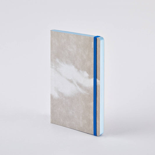 Ein geschlossenes nuuna „Cloud Blue“-Inspirationsbuch in Größe M mit einem grau-weiß marmorierten Einband, das mit einem blauen Gummiband verschlossen ist, steht aufrecht vor einem schlichten weißen Hintergrund.