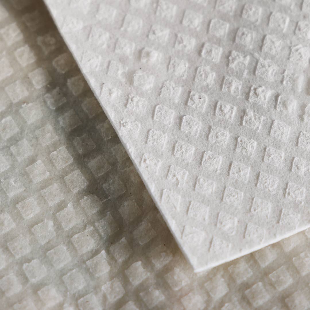 Nahaufnahme von zwei überlappenden "Kranz aus Stiefmütterchen"-Schwammtüchern von More Joy Home, die die weiße, rautenförmige Oberfläche zeigen - ein umweltfreundliches, biologisch abbaubares Zero-Waste-Produkt für nachhaltige Reinigung.
