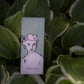 Eine Schachtel Archivist | 'Aloe Vera' Handcreme von Archivist Gallery mit einer illustrierten Frau und dem Text "Aloe Vera" ruht inmitten großer grüner und weißer, panaschierter Blätter.