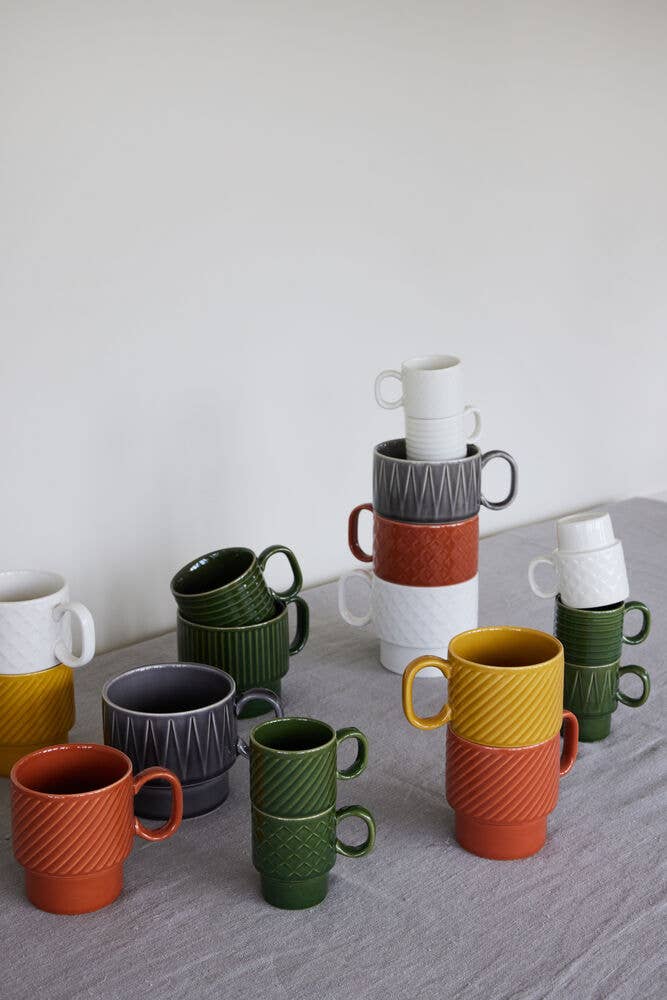 Zwei terrakottafarbene Sagaform Kaffeebecher aus der Coffee & More Serie der Sagaform GmbH sind auf einem grauen Tuch vor einem schlichten weißen Hintergrund gestapelt.