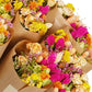 Sträuße aus leuchtenden Trockenblumen in Gelb-, Orange-, Rosa- und Beigetönen sind kunstvoll in braunes Kraftpapier eingewickelt und eng aneinandergebunden – jeder einzelne Strauß unterstreicht den bezaubernden Charme der Kollektion „Wildflowers by Floriette | ‚Summer Crush‘ – Sommer-Bestseller-Trockenblumen“.
