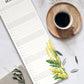 Eine Tasse schwarzer Kaffee auf einer hölzernen Untertasse steht neben dem Wildblumen Atelier | Wandkalender 2026 mit handgezeichneten Blumen, FSC von Wildblumen Atelier, mit schönen gelben Blumen, auf einer weißen Marmorfläche mit einer beigen Serviette und grünen Blättern.
