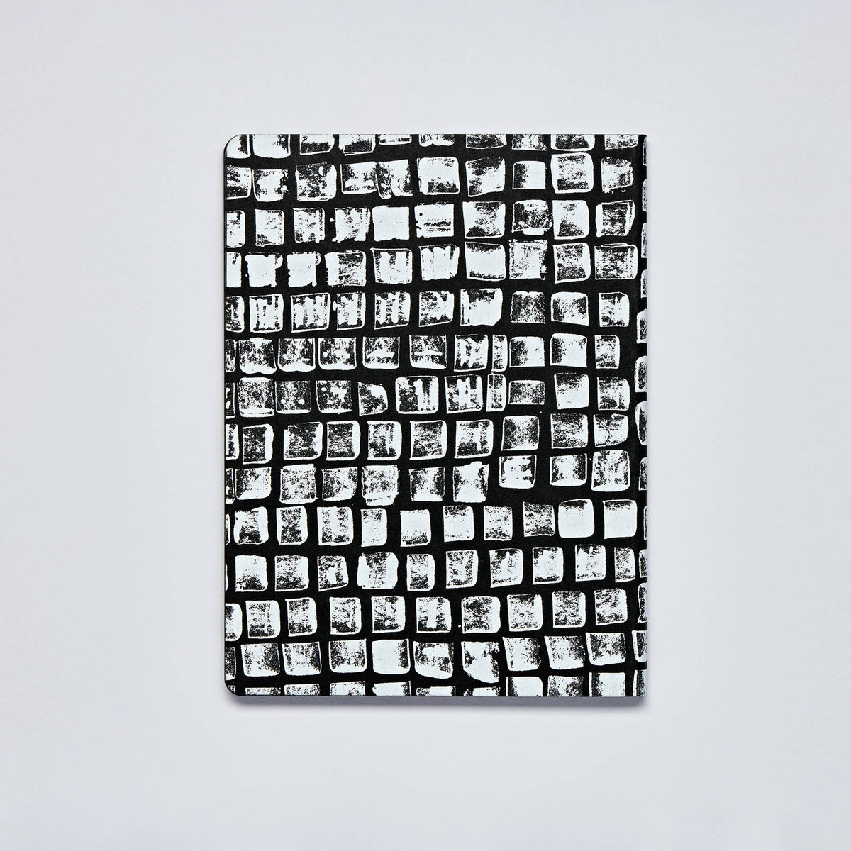 Ein nuuna | „Sassy Squares“ Notizbuch Not Ordinary L Light A5+ mit einem schwarz-weißen Einband, auf dem ein Raster aus groben, unregelmäßigen Quadraten ein abstraktes, handgezeichnetes Muster auf einem schlichten, hellen Hintergrund bildet.