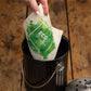 Eine Hand legt das More Joy Home 'Kranz aus Stiefmütterchen' biologisch abbaubares Schwammtuch mit ECO-Label in eine schwarze Komposttonne auf Holz - ein einfacher Schritt zu einem umweltfreundlichen Zero-Waste-Produkt Lifestyle.