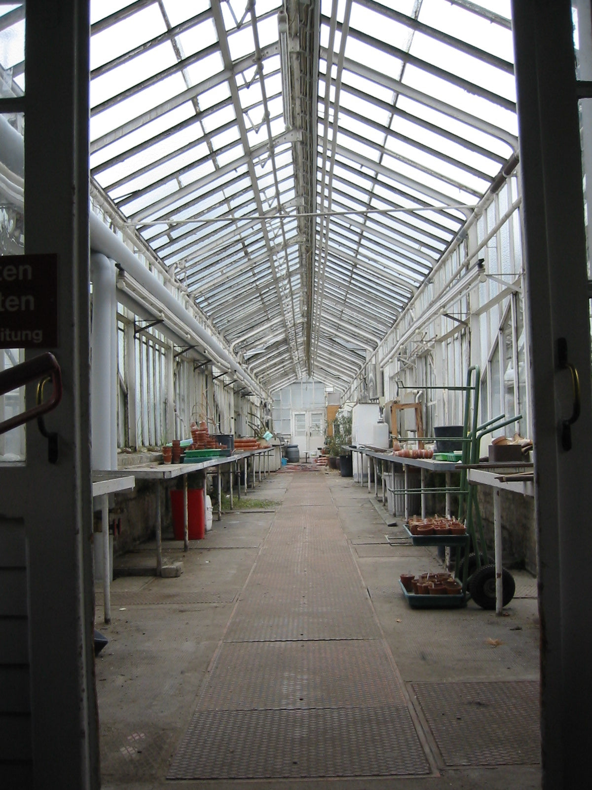 Erleben Sie das üppige, glasüberdachte Gewächshaus der Königlichen Gartenakademie, in dem Arbeitstische und Pflanzen die sonnenbeschienenen Gänge säumen und die Gartenvision von Gabriella Pape verkörpern. Besuchen Sie "LUSTWANDELN" am Fr. 25.09.2026 von 17:00-18:00 Uhr und erkunden Sie mit ihr seine Geschichte.