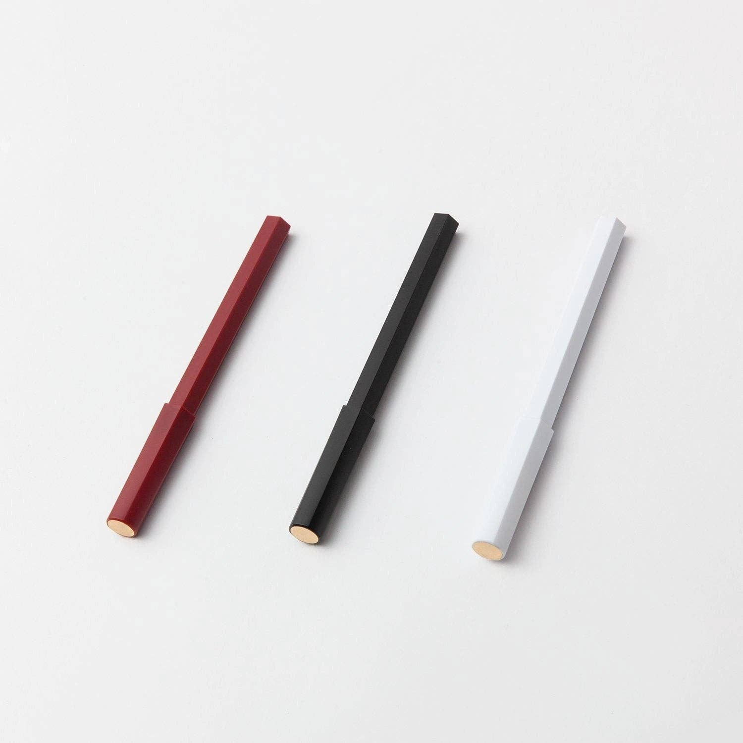 Drei YSTUDIO Harz-Rollerball-Stifte (Weiß) von ENTREPÔT sind diagonal auf einer weißen Fläche angeordnet, ihre sechseckigen Körper sind elegant und die Spitzen zeigen nach links unten.