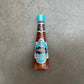 Eine Flasche Firelli | Extra scharfe italienische Sauce 148 ml mit blauem Deckel steht auf einer grauen Fläche. Die italienische Sauce von Firelli, mit kalabrischen Chilischoten, passt perfekt zu Grillfleisch. Das Etikett ist blau, schwarz und rot.