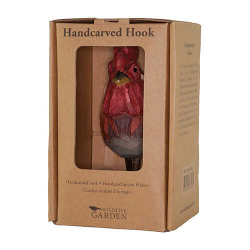 Eine Pappschachtel mit Klarsichtfenster zeigt den Wildlife Garden | Handgeschnitzter Wandhaken aus Holz 'Hahn'. Die Verpackung ist mit "Handgeschnitzter Wandhaken" und "Wildlife Garden" beschriftet und enthält mehrsprachige Produktbeschreibungen.