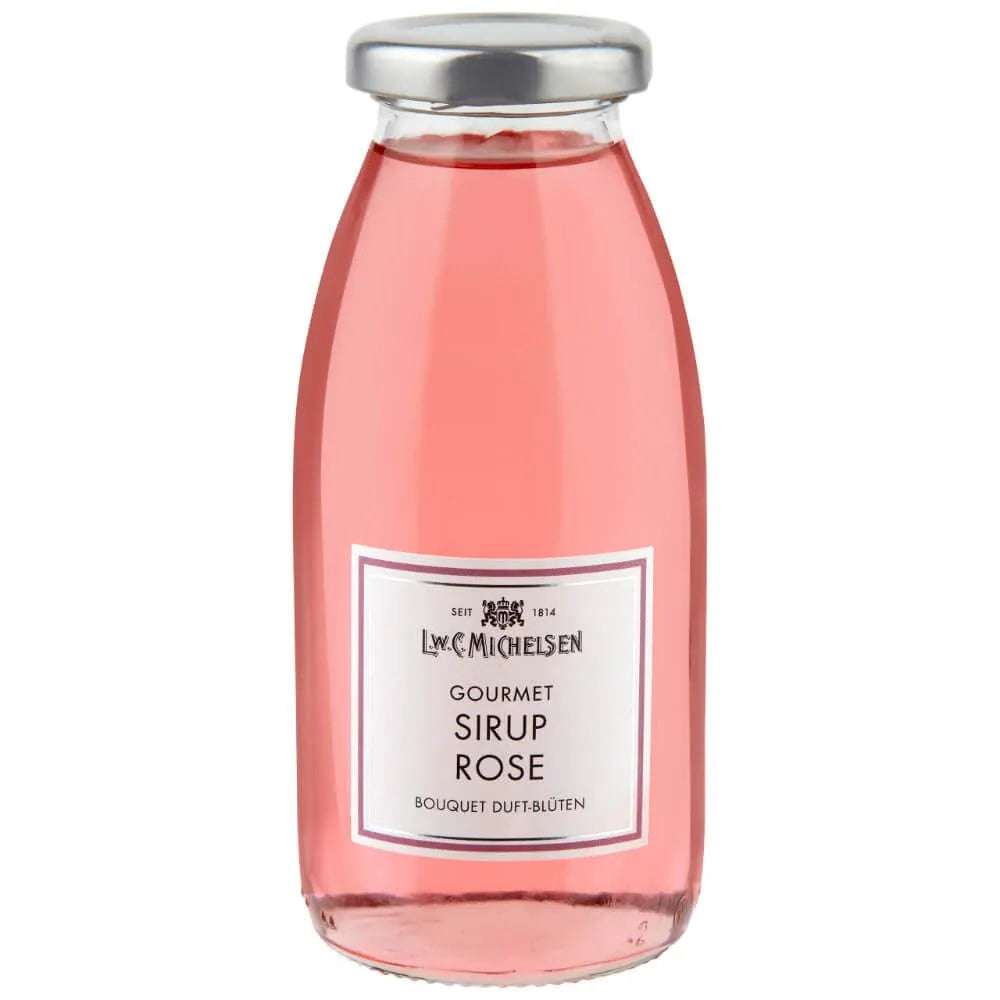 Eine klare Glasflasche, gefüllt mit rosa Rosensirup, verschlossen mit einem silbernen Verschluss. Auf dem Etikett ist die Marke L.W.C. Michelsen abgebildet und die Aufschrift „Gourmet Sirup Rose 250 ml“ zu lesen, was die gleiche Eleganz widerspiegelt wie die renommierte Kollektion des Unternehmens.
