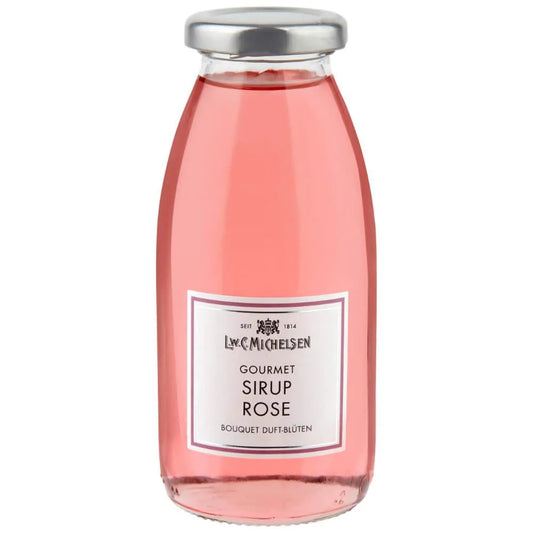 Eine klare Glasflasche, gefüllt mit rosa Rosensirup, verschlossen mit einem silbernen Verschluss. Auf dem Etikett ist die Marke L.W.C. Michelsen abgebildet und die Aufschrift „Gourmet Sirup Rose 250 ml“ zu lesen, was die gleiche Eleganz widerspiegelt wie die renommierte Kollektion des Unternehmens.