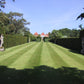 Ein langer, gestreifter Traumrasen für den Workshop der Königlichen Gartenakademie Sa., 6.3.2027 | 10.00 – 12.00 Uhr WORKSHOP Haben Sie schon Rasen oder immer noch Gras?, flankiert von hohen Hecken und Steinstatuen.