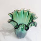 Die „Murano Dream Große ‚Fazzoletto‘-Vase“ aus grünem Murano-Glas (H 32, Ø 24 cm) mit gewellten, geriffelten Rändern und einer durchscheinenden Oberfläche steht auf einer weiß-grauen Marmorfläche vor einem schlichten Hintergrund.