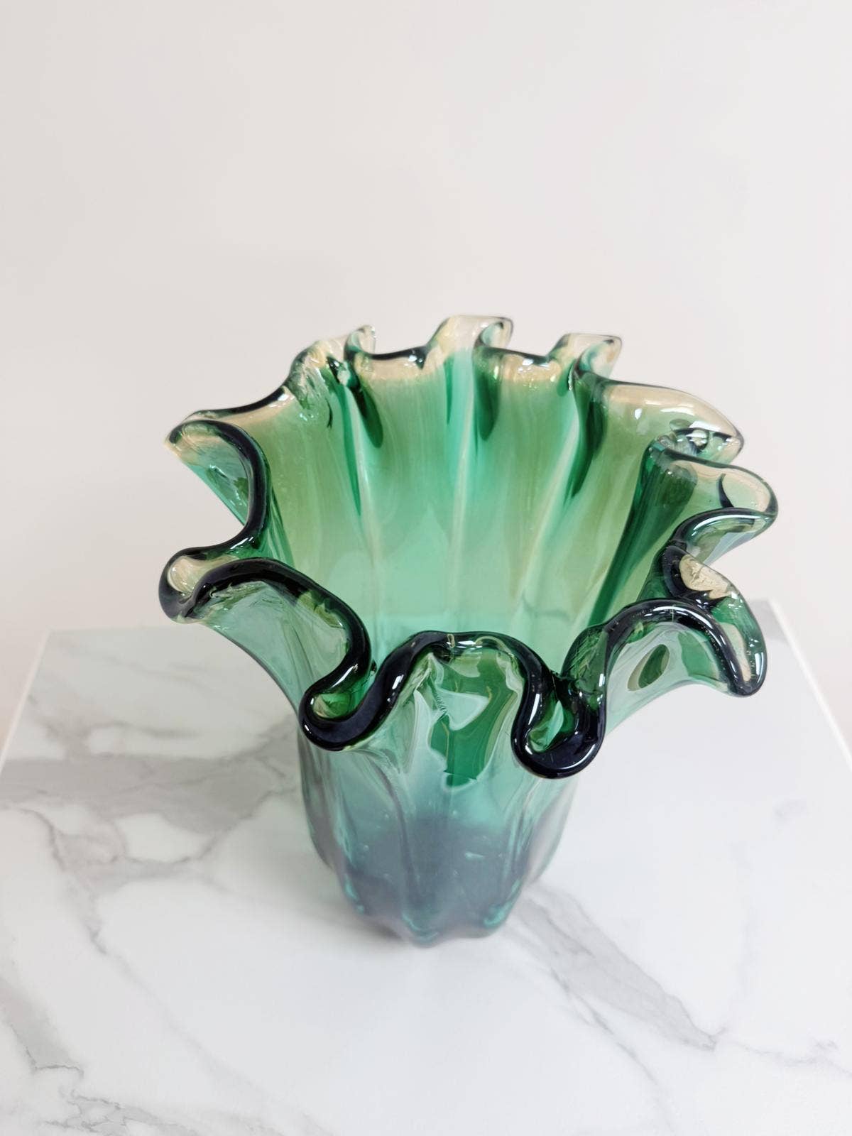 Die „Murano Dream Große ‚Fazzoletto‘-Vase“ aus grünem Murano-Glas (H 32, Ø 24 cm) mit gewellten, geriffelten Rändern und einer durchscheinenden Oberfläche steht auf einer weiß-grauen Marmorfläche vor einem schlichten Hintergrund.