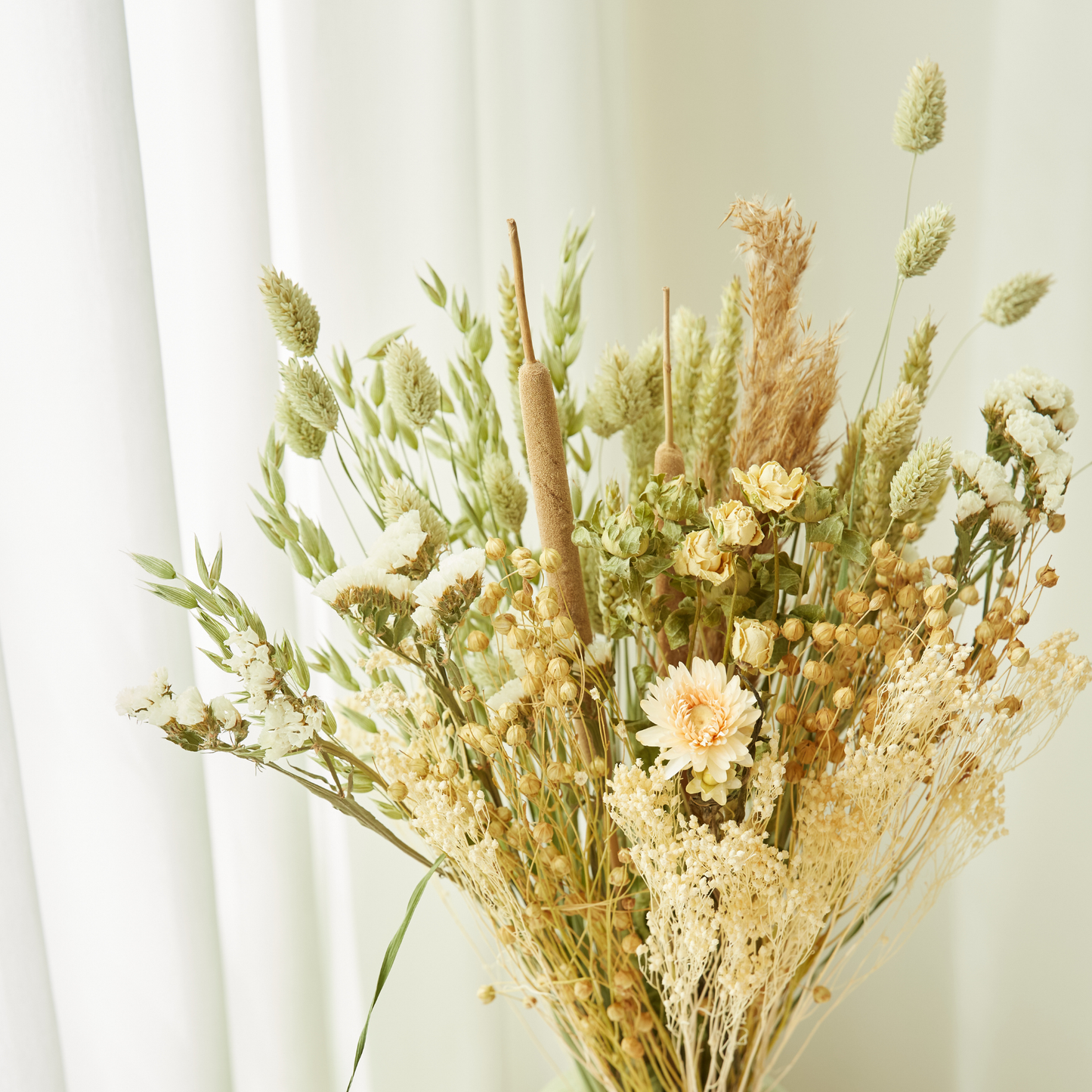 Ein getrockneter Feldblumenstrauß – „Getrockneter Feldblumenstrauß ‚Natur‘“ in Größe M von Wildflowers by Floriette – mit Weizen, Rohrkolben und zarten Wildblumen, arrangiert vor einem sanften weißen Vorhang als Hintergrund.