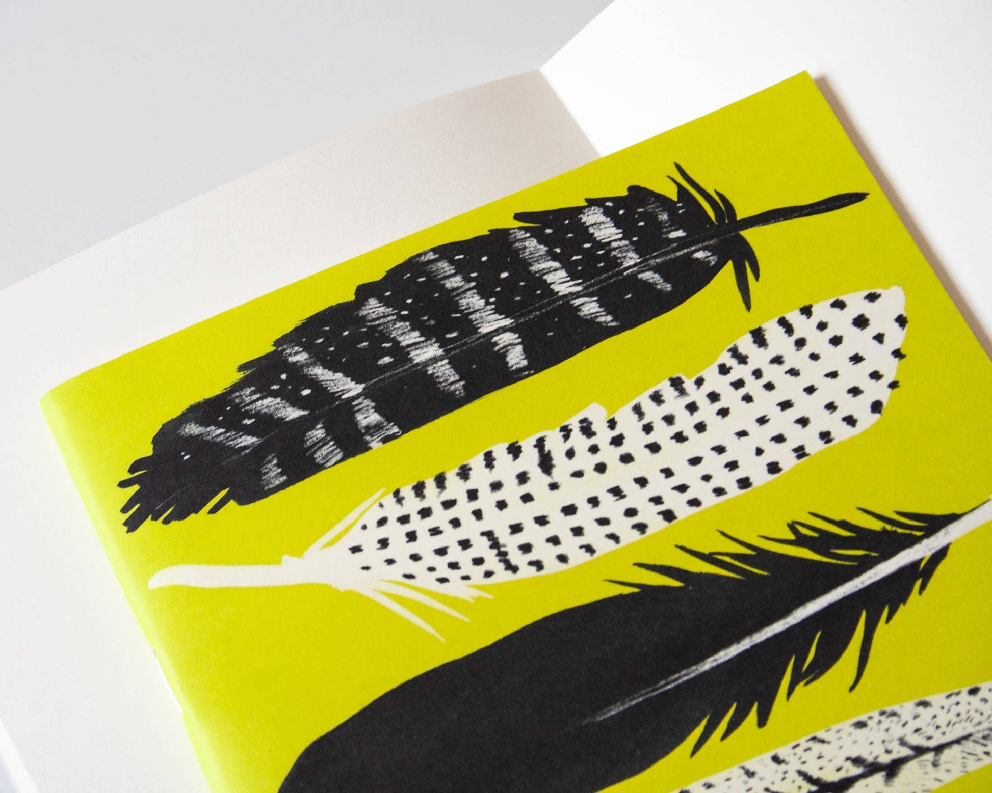 Eine Nahaufnahme des Papaya Paper Products | Schönes Notizheft A5 mit Federn in gelb zeigt schwarz-weiß illustrierte Federn mit verschiedenen Mustern auf einem leuchtend gelben Einband, hergestellt von Papaya Paper Products.