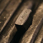 Nahaufnahme des ENTREPÔT YSTUDIO Klassische Renaissance KAZARI KANAGU ORCHID Tintenroller, dessen rechteckiger Metallkörper mit verschnörkelten Gravuren versehen ist und der neben anderen ähnlichen Metallschreibern ausgestellt ist.
