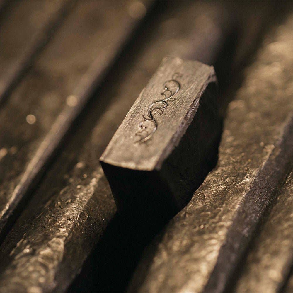 Nahaufnahme des ENTREPÔT YSTUDIO Klassische Renaissance KAZARI KANAGU ORCHID Tintenroller, dessen rechteckiger Metallkörper mit verschnörkelten Gravuren versehen ist und der neben anderen ähnlichen Metallschreibern ausgestellt ist.