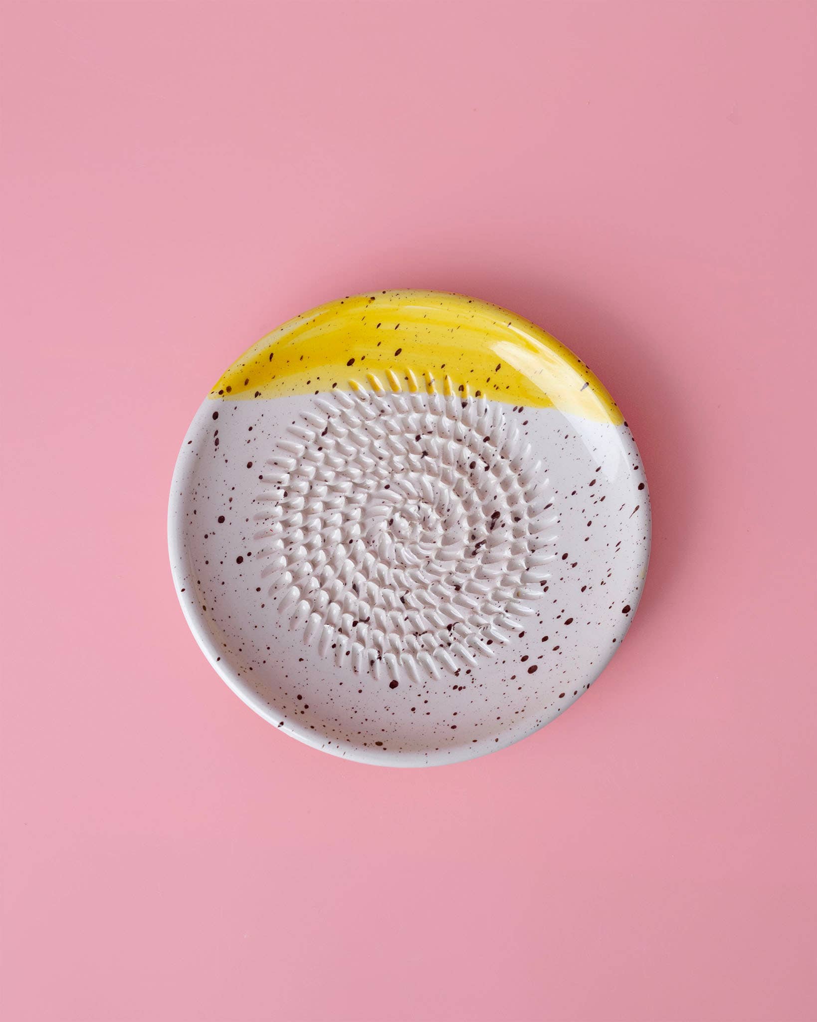Der Alfar Tierra Cocida | Kleiner Keramikreibe Teller ZIMT ist ein handgefertigter runder Keramikteller mit strukturierter Mitte, weißem Boden, schwarzen Sprenkeln und gelbem Randbereich, abgebildet auf einem rosa Hintergrund.