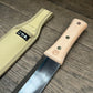Das Niwaki | 'Hori Hori' multifunktionales Pflanzmesser mit Holzgriff und Metallklinge liegt neben der Schutzhülle aus Stoff mit schwarzem Etikett und weißen japanischen Schriftzeichen - ideal für die Gartenarbeit.