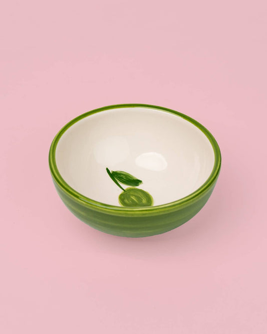 Die kleine Keramikschale „Olive“ von Alfar Tierra Cocida präsentiert sich in Grün und Weiß mit einem filigranen Blatt- und Fruchtmotiv auf der Innenseite, handgefertigt in Spanien und auf einem zarten rosafarbenen Hintergrund.