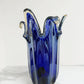 Die „Murano Dream“ | Die große „Giusy“-Vase aus blauem, originalem Murano-Glas (H 32, Ø 20 cm) besticht durch ihren gewellten Rand und goldene Akzente – ein handgefertigtes Kunstwerk vor weißem Hintergrund auf Marmor.