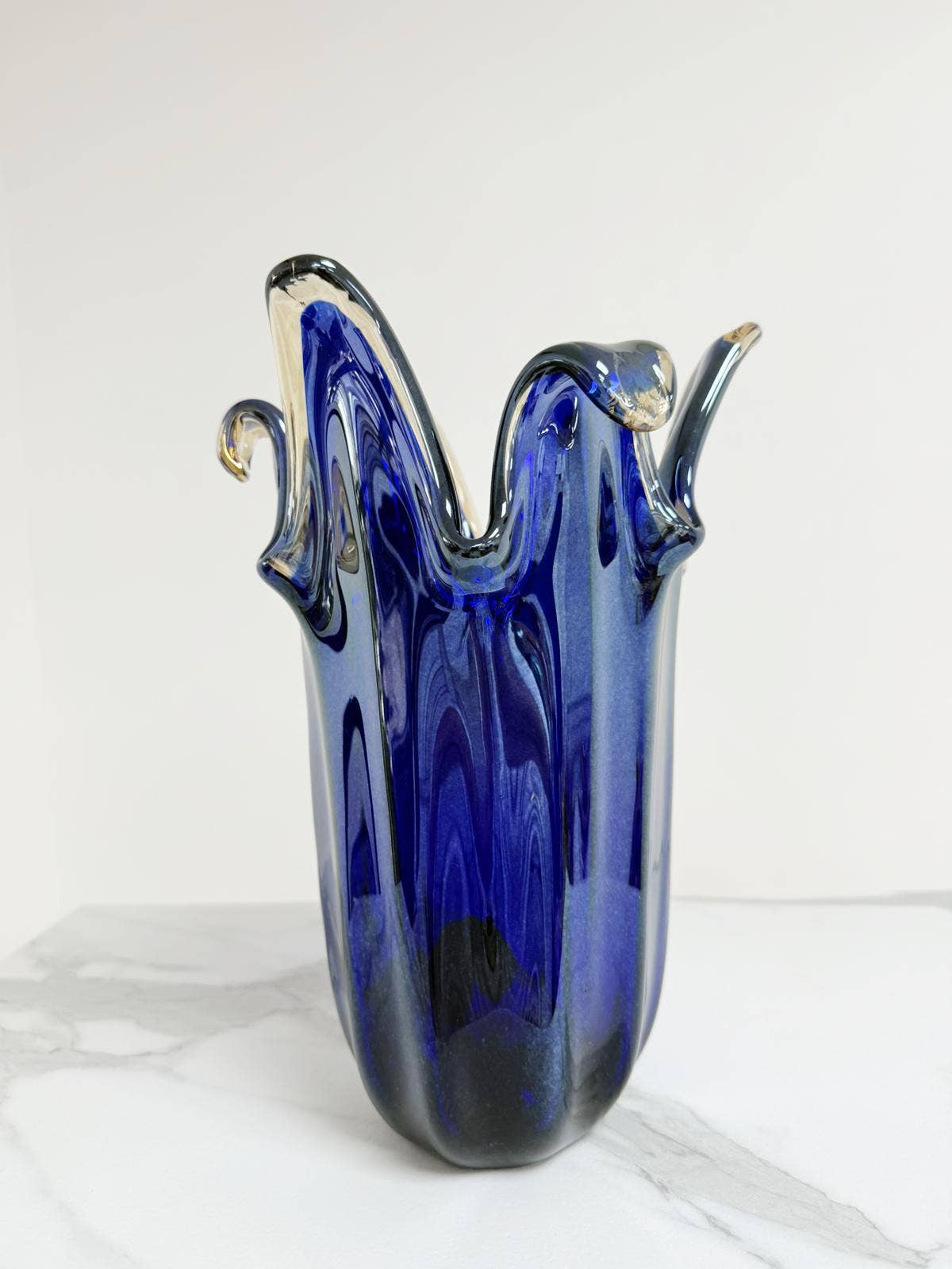 Die „Murano Dream“ | Die große „Giusy“-Vase aus blauem, originalem Murano-Glas (H 32, Ø 20 cm) besticht durch ihren gewellten Rand und goldene Akzente – ein handgefertigtes Kunstwerk vor weißem Hintergrund auf Marmor.