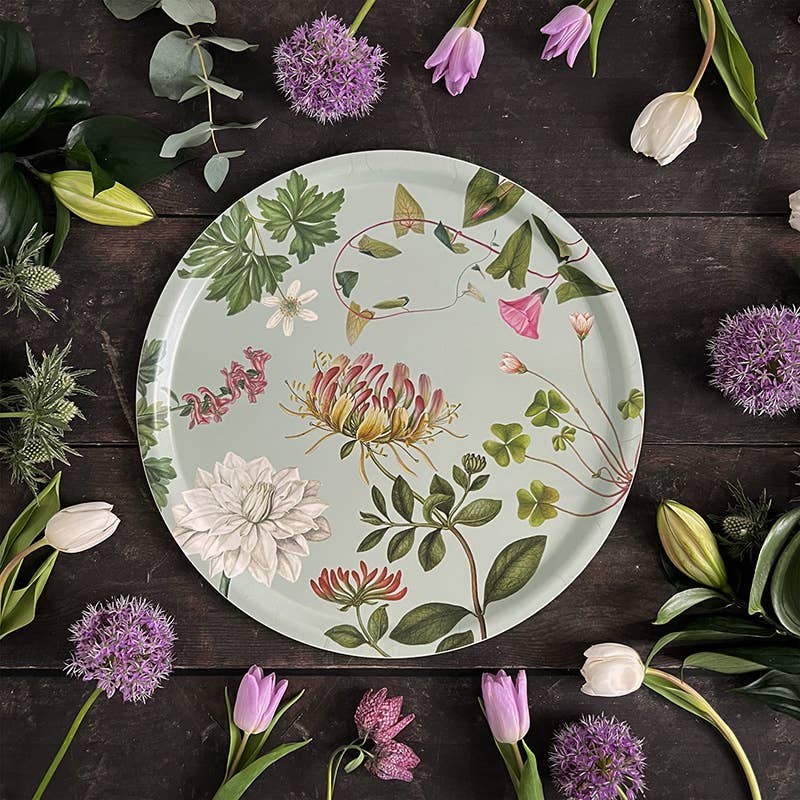 Ein Koustrupco | Das Serviertablett „Flora Danica Atlas“ mit einem Durchmesser von 38 cm, verziert mit illustrierten Blumen und Grünpflanzen, ruht auf einer dunklen Holzfläche, umrandet von Tulpen, Lauchblüten und üppigem Grün, wodurch das botanische Design elegant zur Geltung kommt.